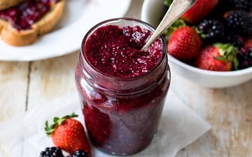 Easy mixed berry chia jam in small curved jar, spoon in the jar, berries in background