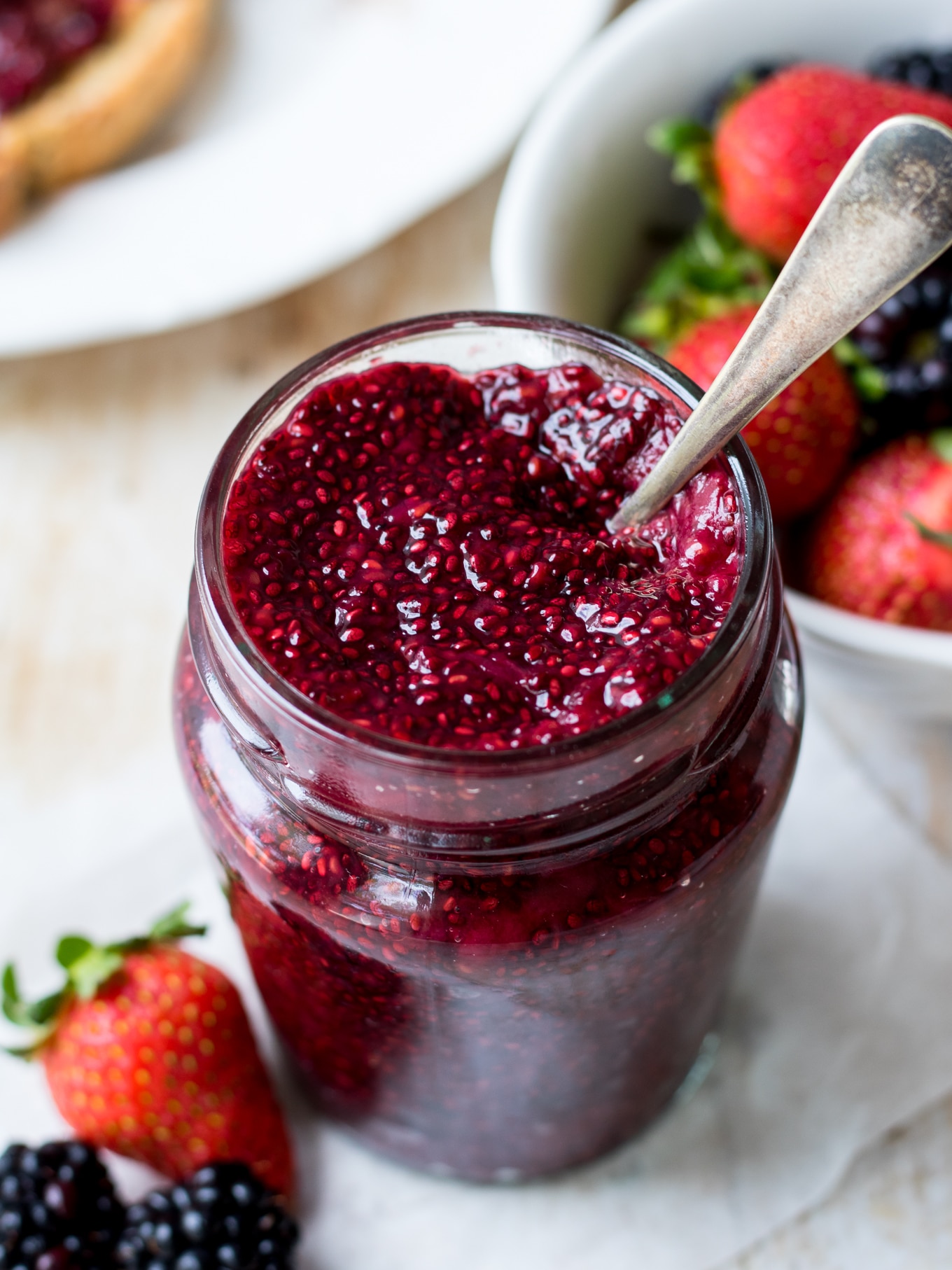 Close up easy mixed berry chia jam in glass jar with spoon sticking out the top.
