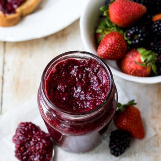 Easy mixed berry chia jam in a small glass jar, side angle with bowl of berries in background.