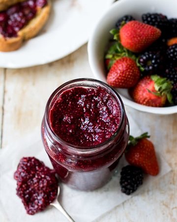 Easy mixed berry chia jam in a small glass jar, side angle with bowl of berries in background.