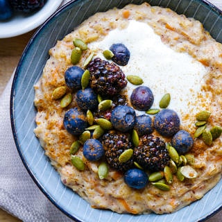 Healthy carrot cake porridge in blue bowl with blueberries and pumpkin seeds