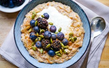 Carrot cake porridge in blue bowl with blueberries and pumpkin seeds