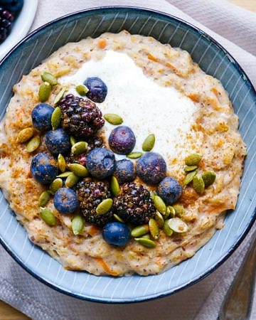 Carrot cake porridge in blue bowl with blueberries and pumpkin seeds