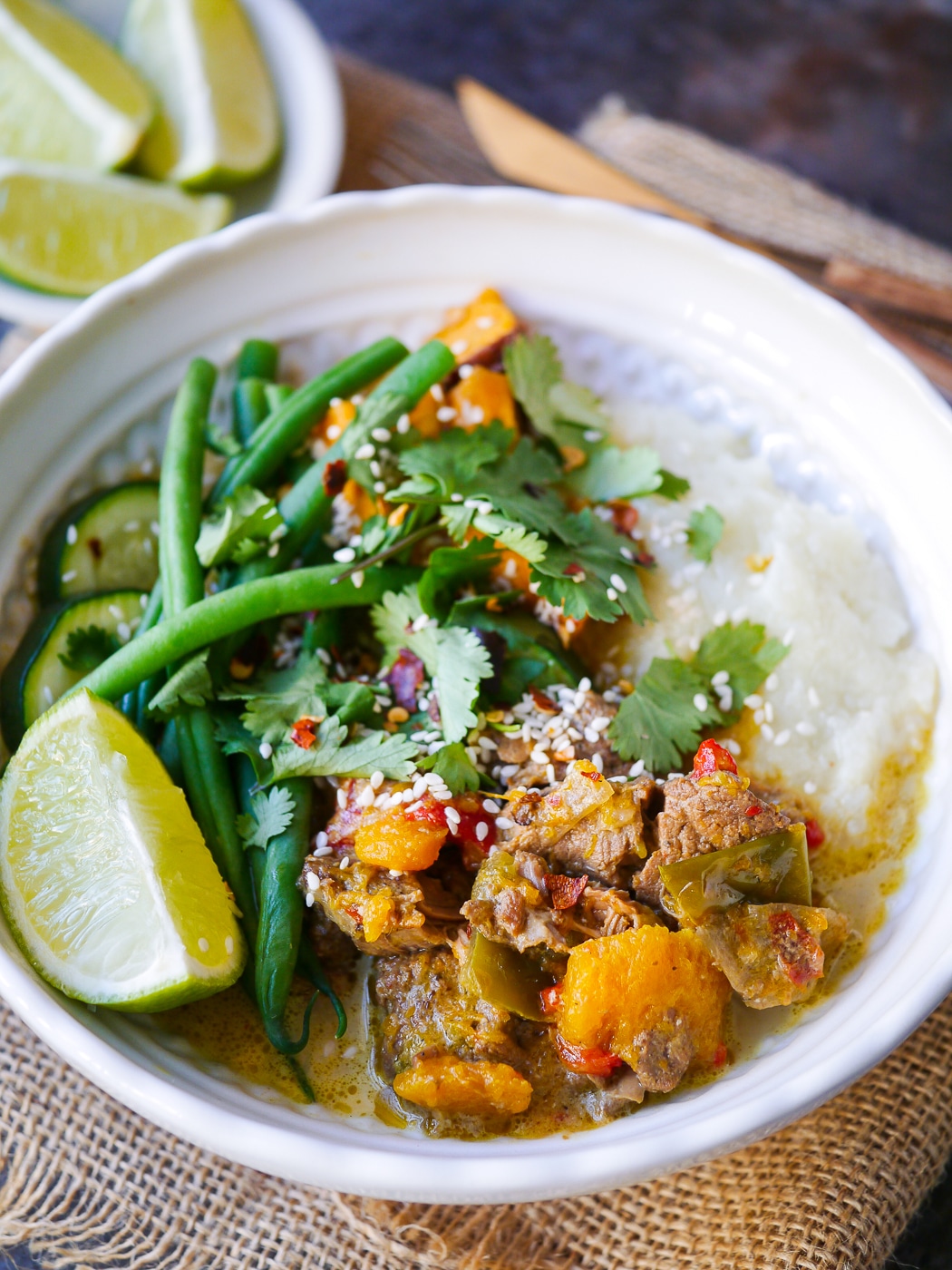 Pumpkin lamb slow cooker curry in a white bowl with fresh green beans and lime wedge