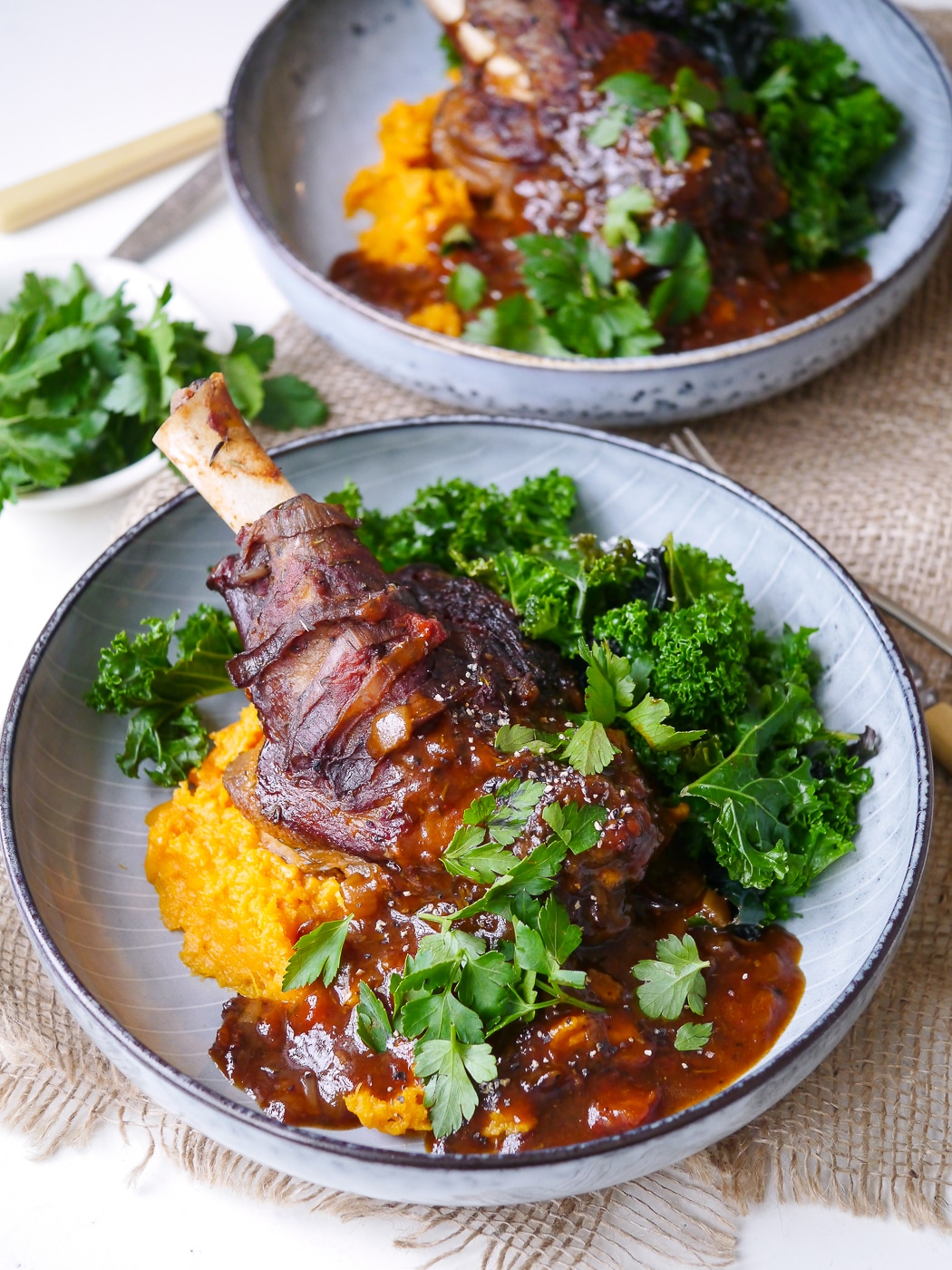 Balsamic slow cooker lamb shank on top of sweet potato mash with kale, blue bowl