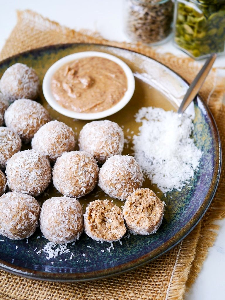 No food processor protein balls rolled in desiccated coconut on a ceramic plate with peanut butter