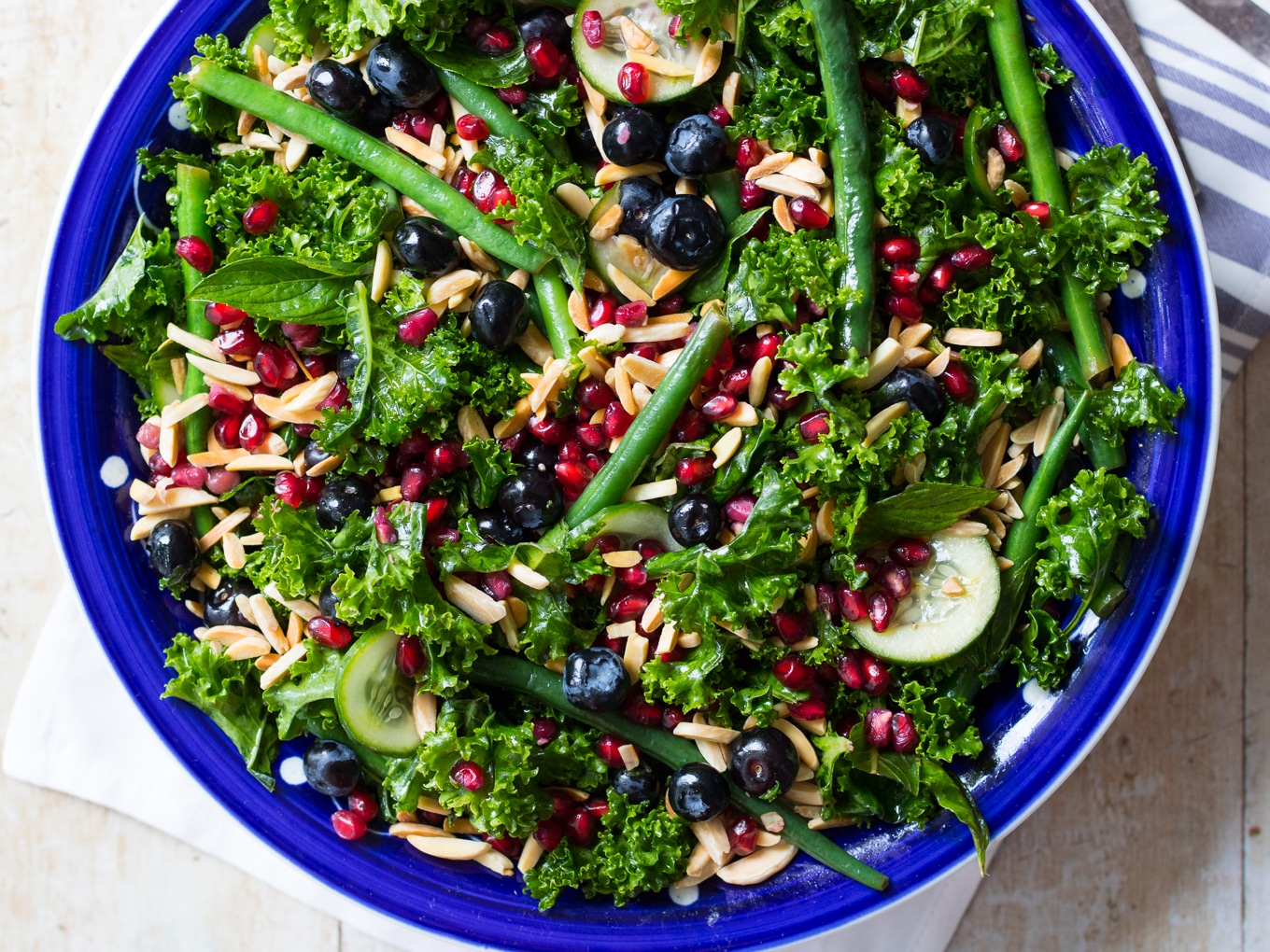 Blueberry kale salad recipe made with massaged kale in olive oil, green beans, cucumber, mint, blueberries, pomegranate and toasted almonds.