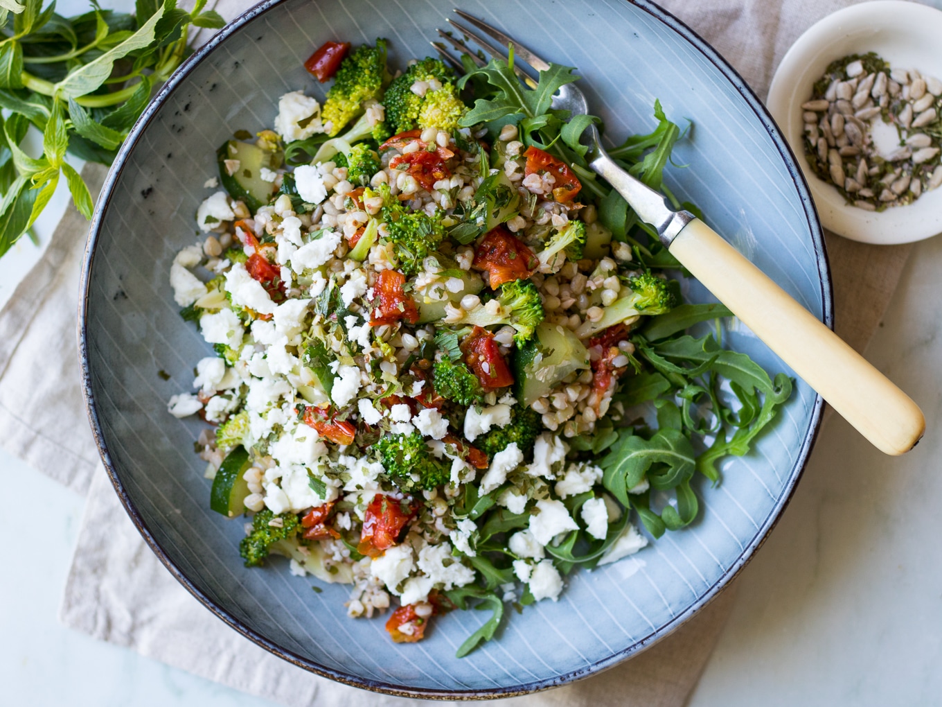 Broccoli Buckwheat Salad with chopped semi dried tomatoes topped with feta cheese in bowl - recipe by Nourish Every Day