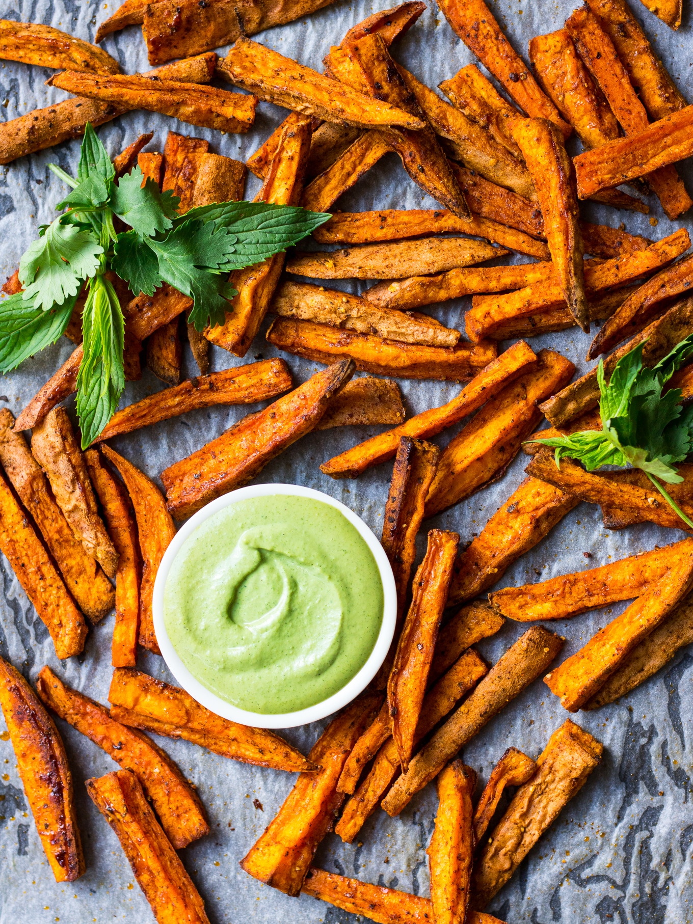 Cinnamon Paprika Sweet Potato Fries roasted on a baking tray, with dipping sauce and fresh mint.