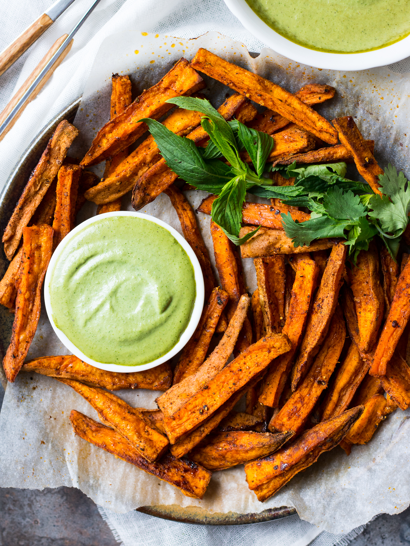 Cinnamon Paprika Sweet Potato Fries arranged on plate with green herb dipping sauce.