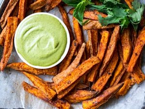 Cinnamon Paprika Sweet Potato Fries arranged on a plate with dipping sauce and herbs.