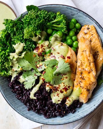 Chicken black rice bowl, one blue serving bowl filled with rice, marinated chicken, broccolini, peas and creamy herb sauce