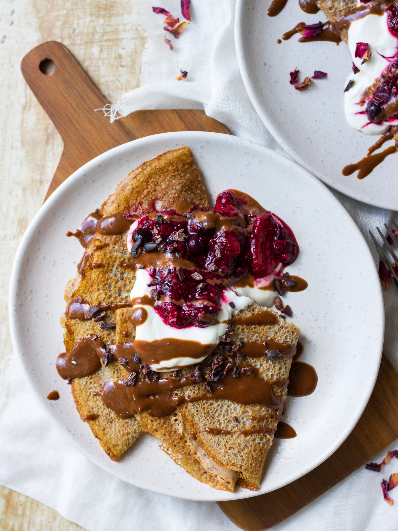 Sweet vegan buckwheat crepes folded in quarters, topped with yoghurt, berry sauce and chocolate sauce drizzle.