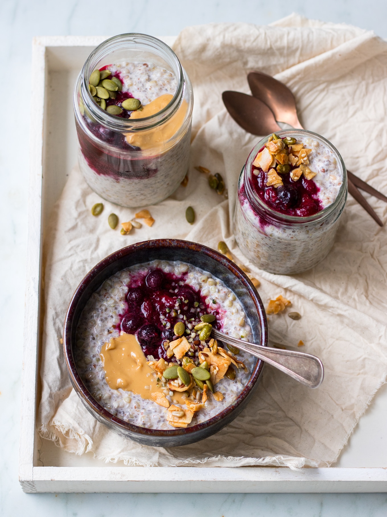 One bowl and two jars of buckwheat bircher, topped with berries and granola