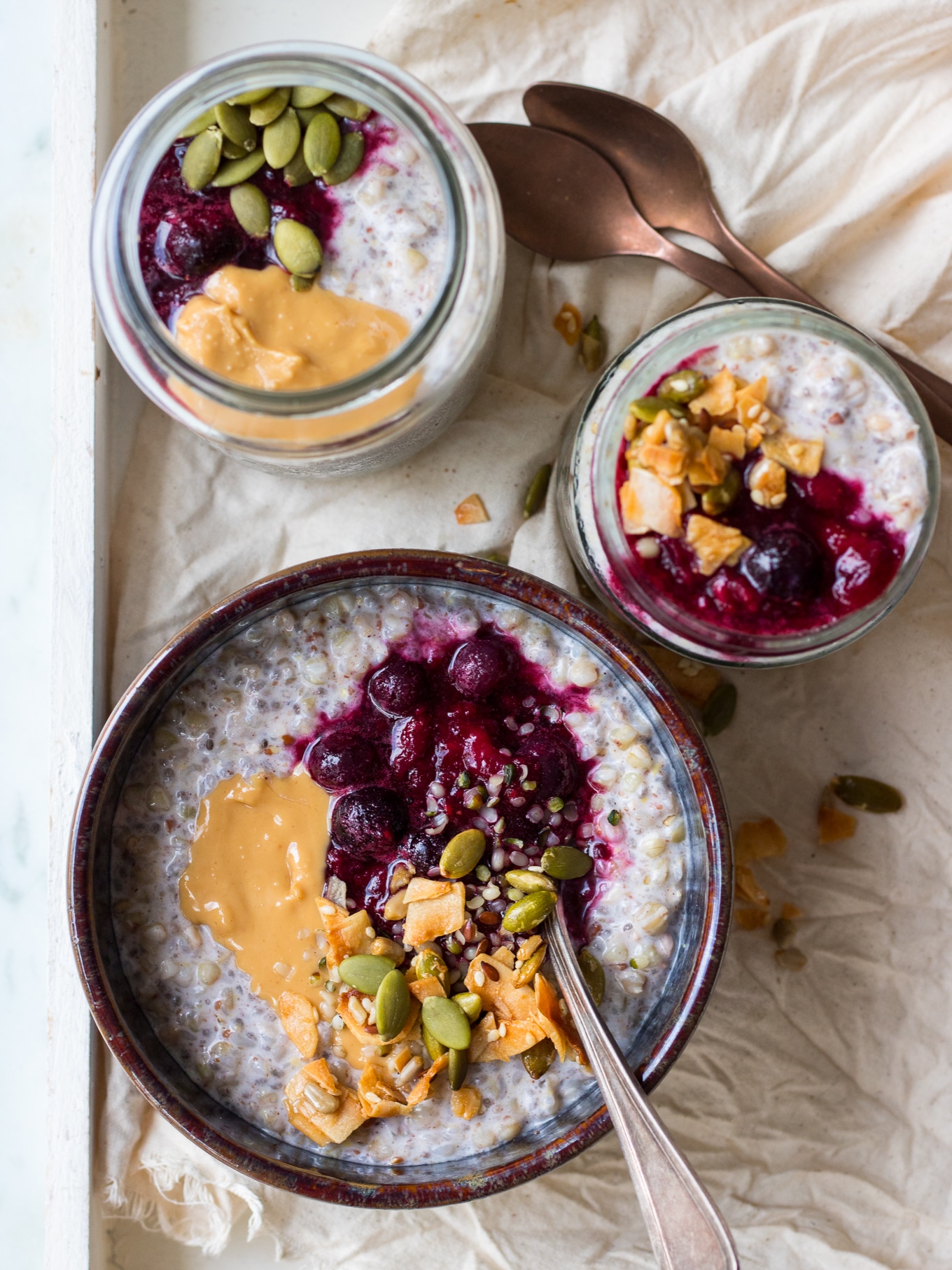 Three jars and bowls of buckwheat bircher on a cream background, top down view