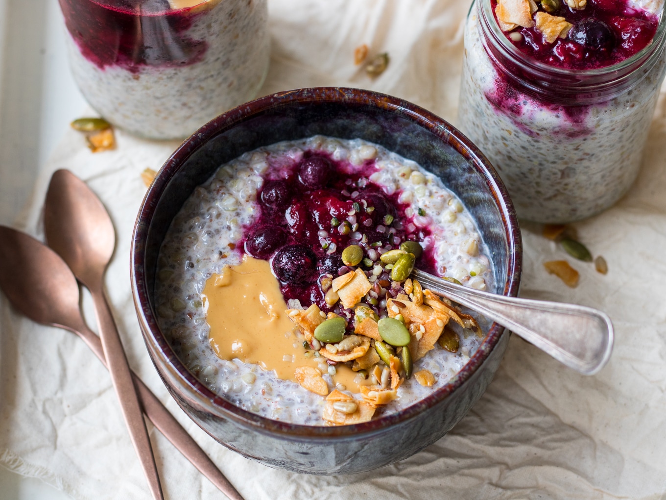 Buckwheat bircher in a small blue ceramic bowl, berries, nut butter and granola on top