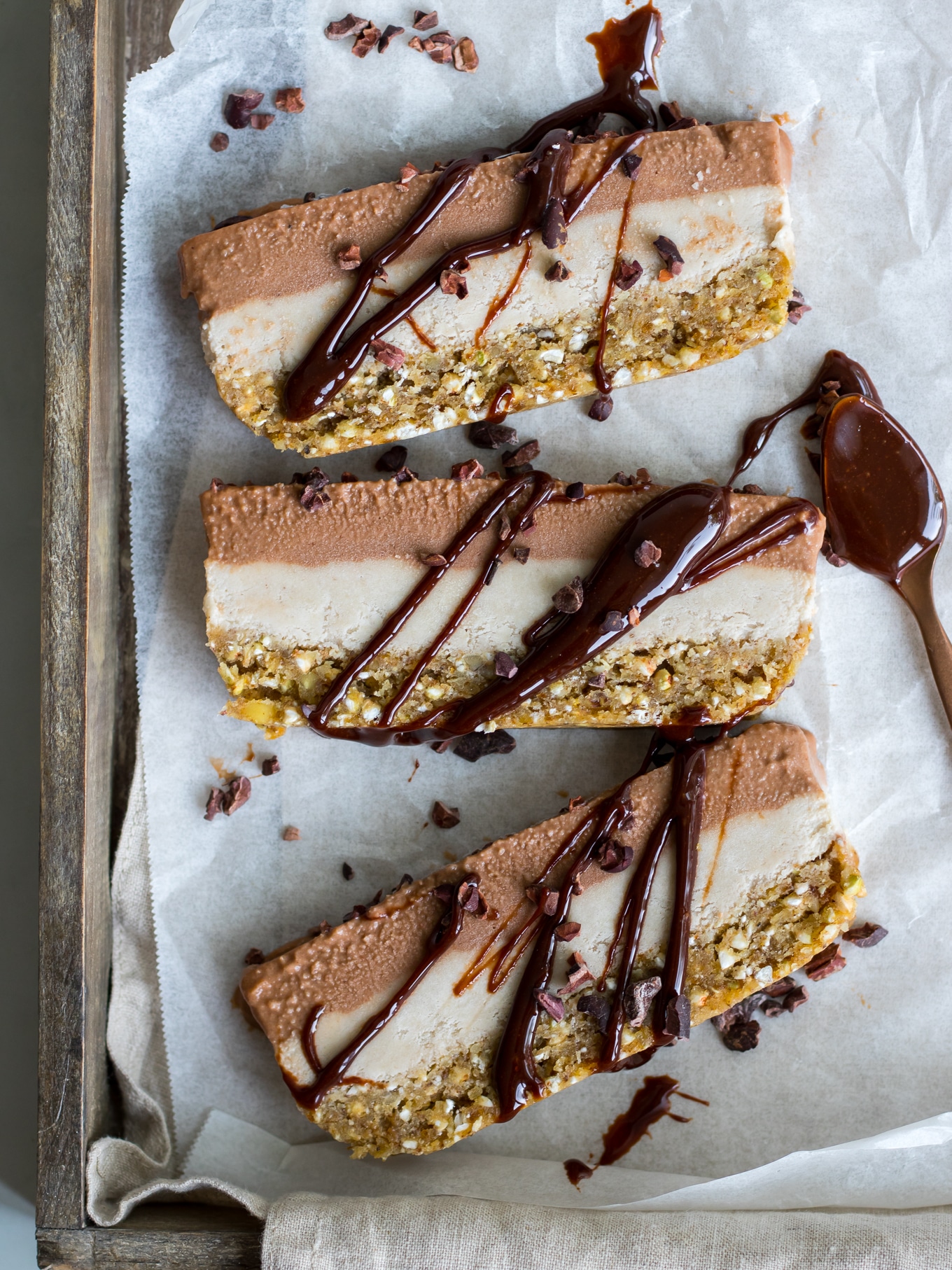 Vegan chocolate banana nice cream cake slices on white baking paper, chocolate sauce drizzled on top, wooden tray