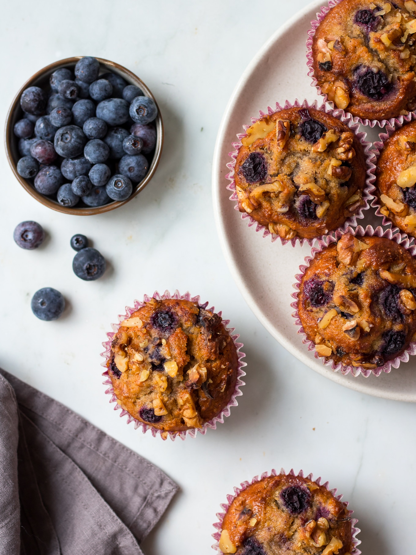 Healthy Blueberry Cinnamon Muffins on white backdrop, with bowl of blueberries