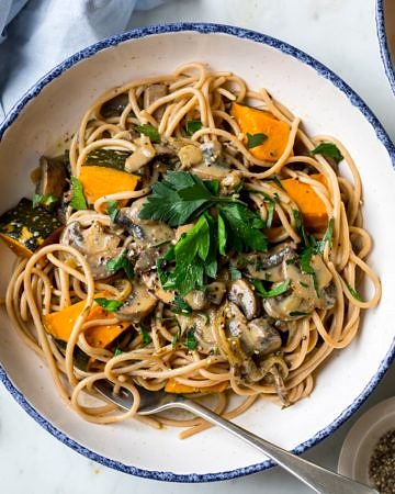 vegan mushroom pasta with roast pumpkin chunks and parsley garnish, white bowl with blue rim