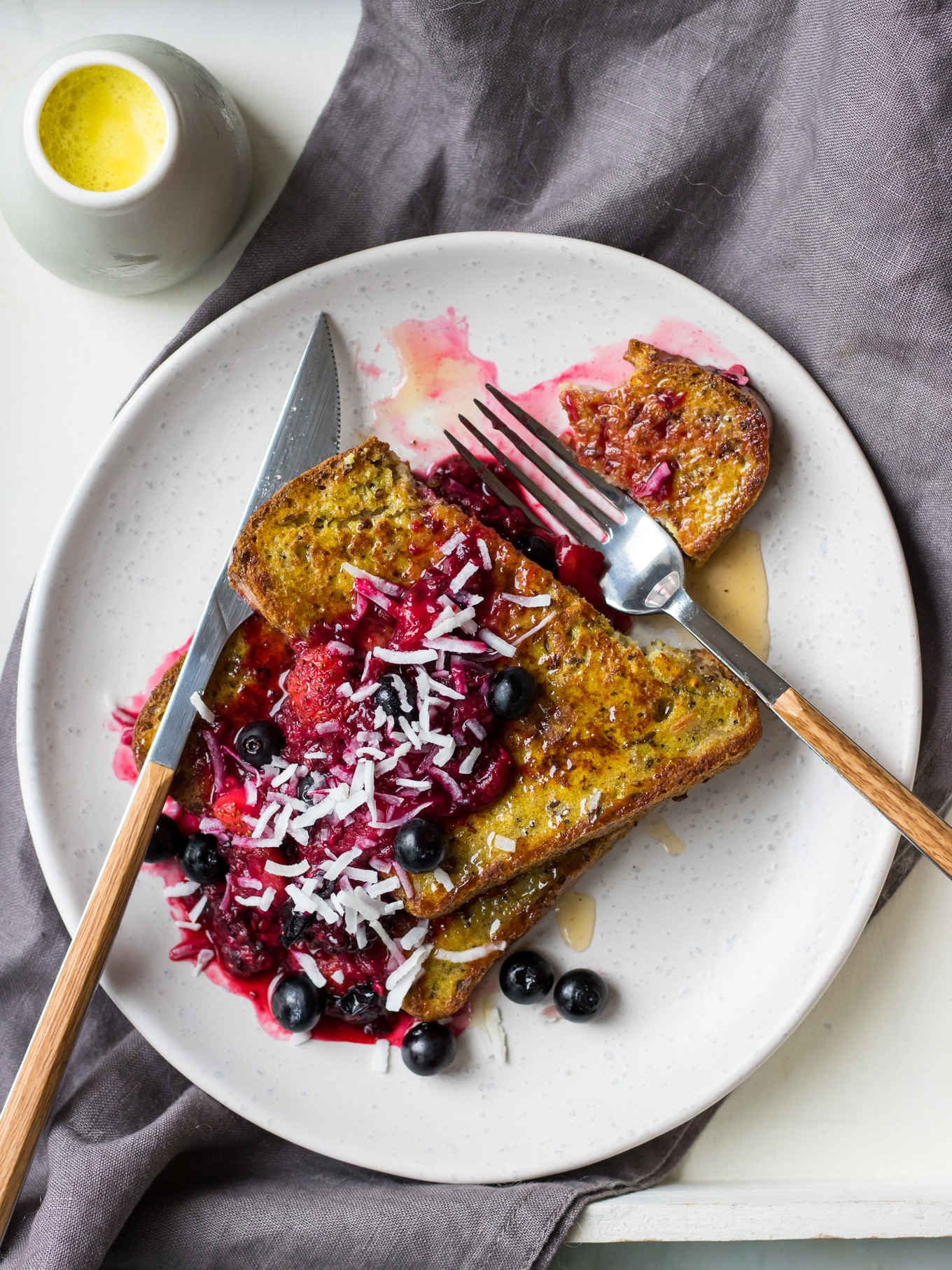 Golden milk french toast stacked on a white plate topped with berry compote and flaked coconut.