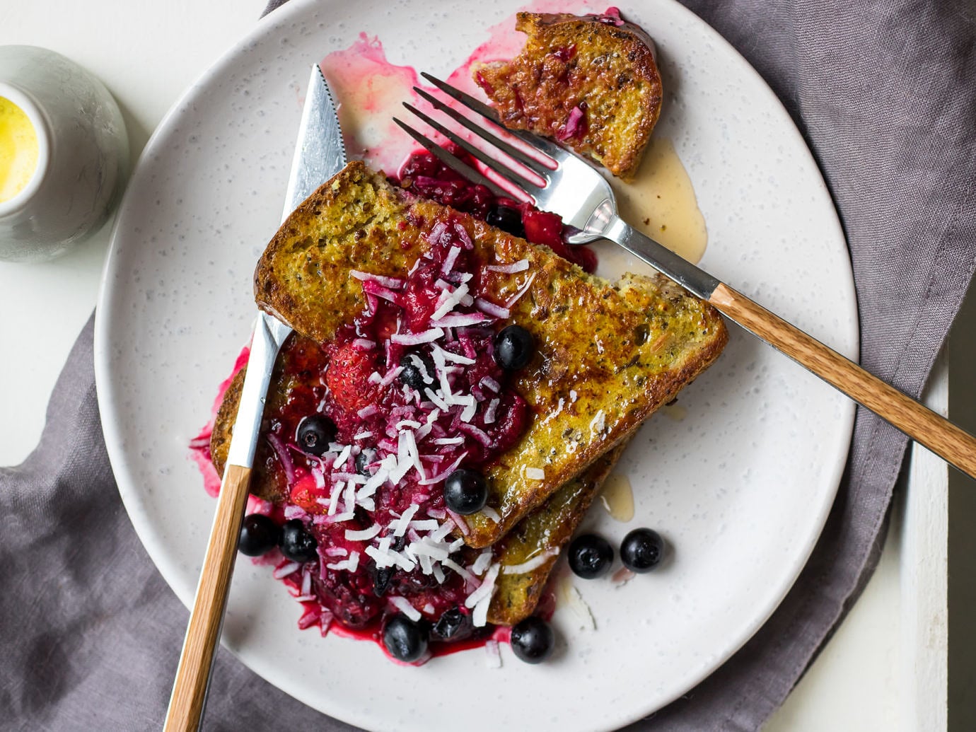 Golden milk french toast stacked on a white plate topped with berry compote and flaked coconut.