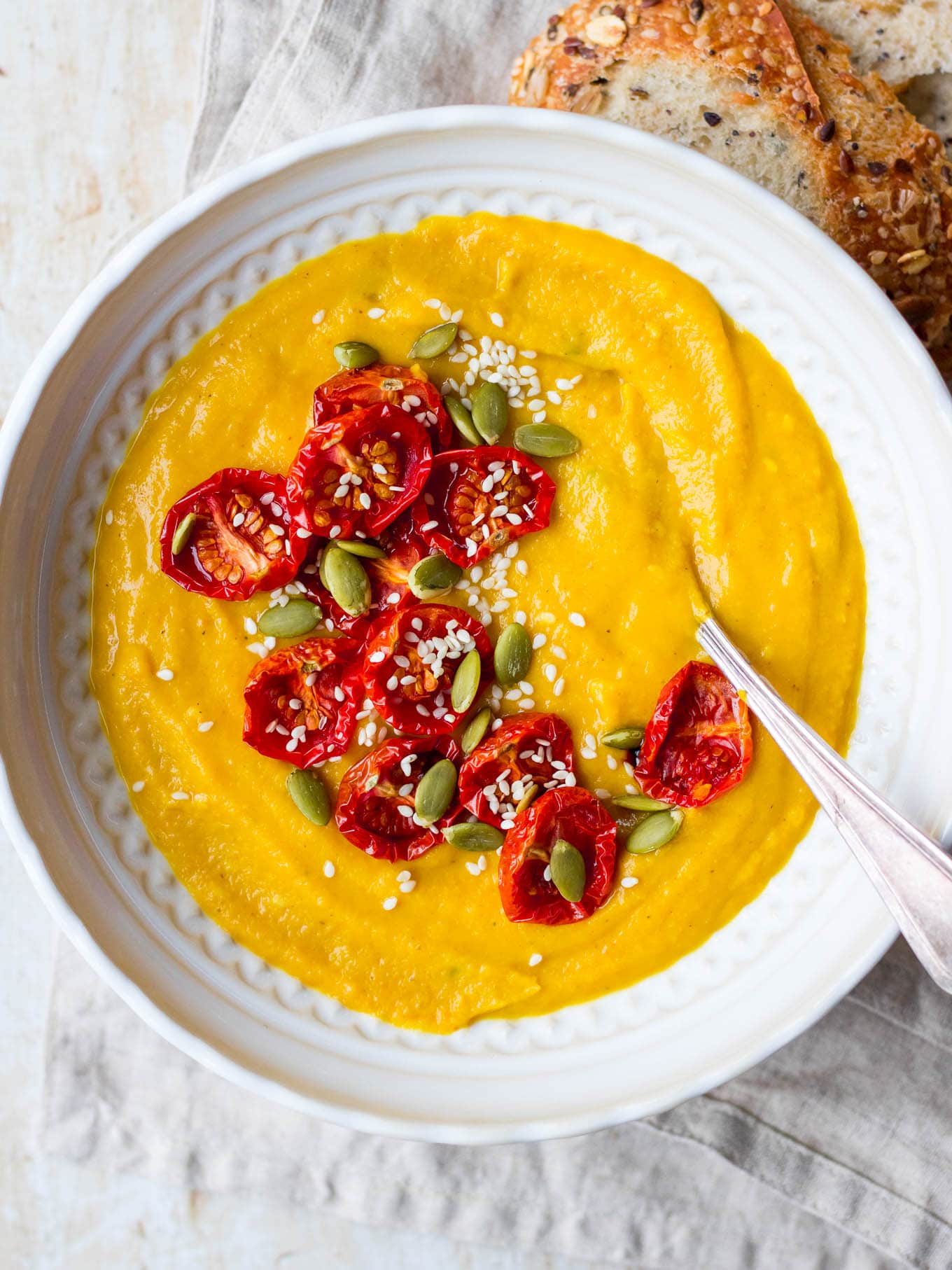 Cauliflower, sweet potato and red lentil soup in white patterned bowl with slow roasted tomatoes