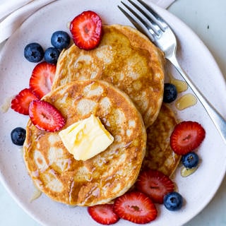 gluten free buckwheat pancakes on a white ceramic plate with fresh berries and maple syrup