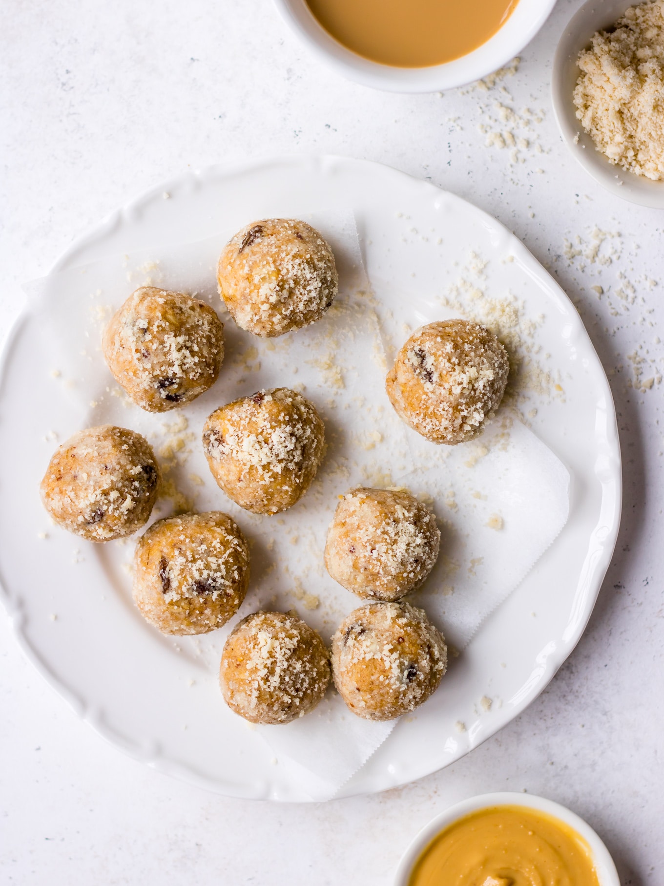 Lactation Bites bliss balls arranged on a white irregular plate, scattered with almond meal