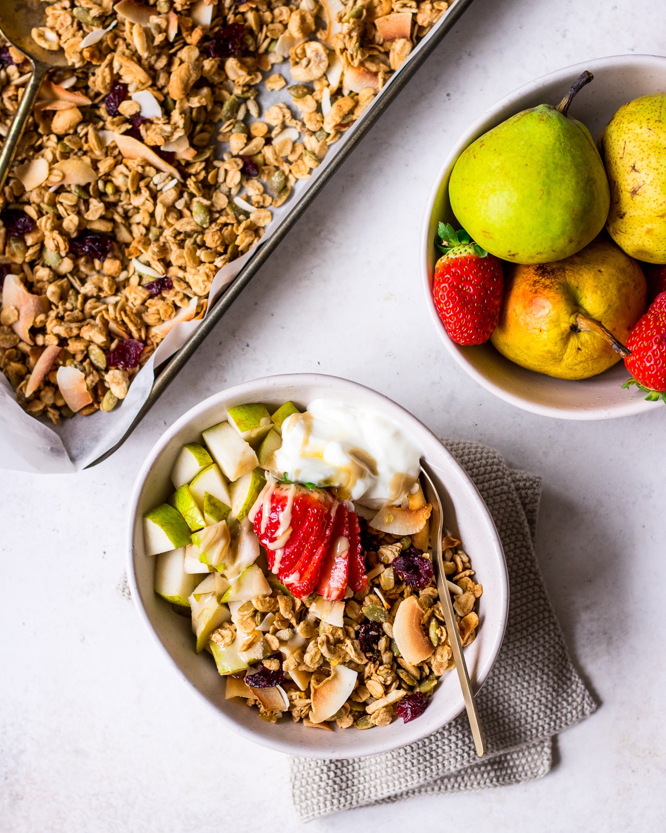 Maple tahini granola on a tray and served in a bowl with pear and strawberries