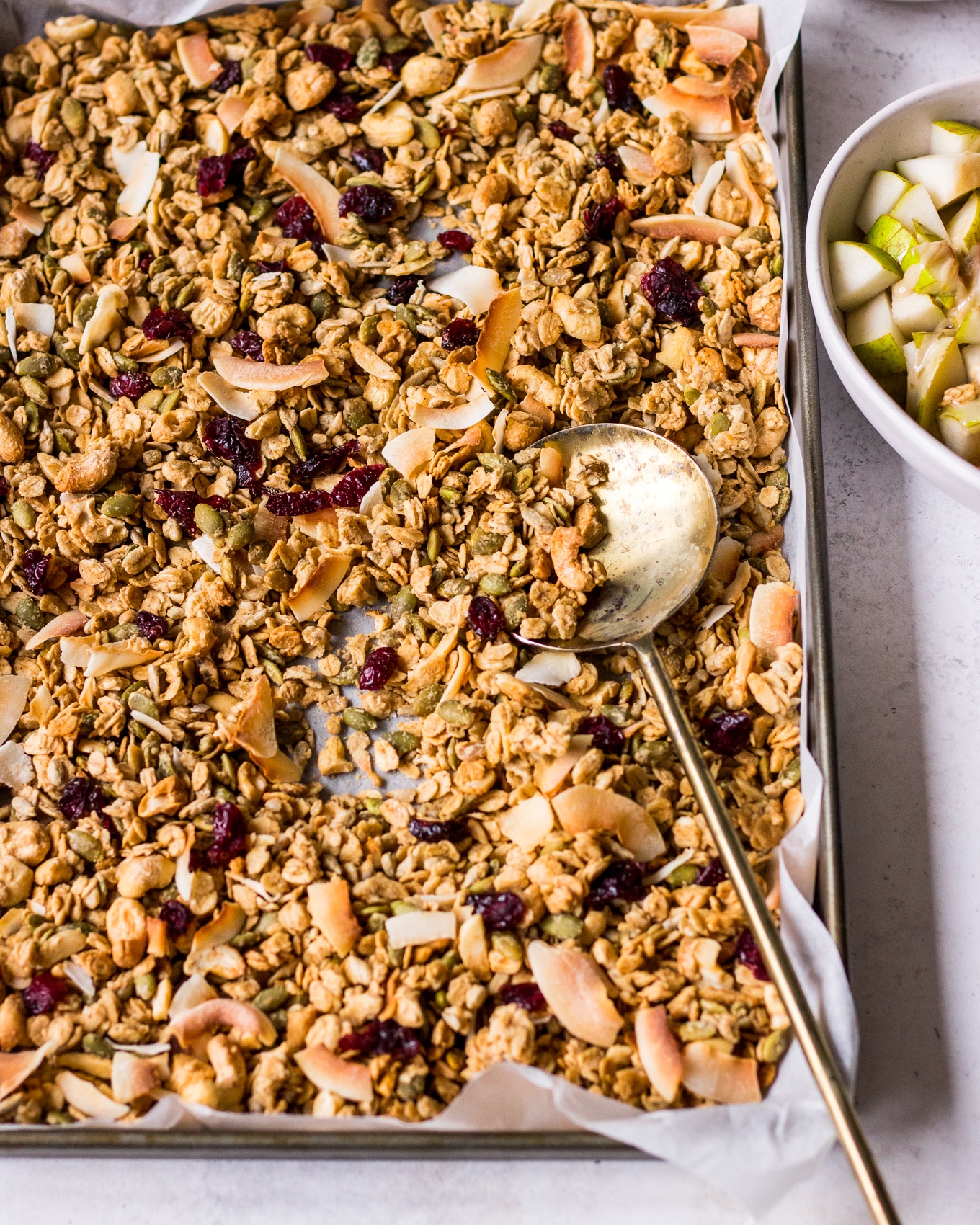 Angle shot of tray of tahini granola with gold spoon