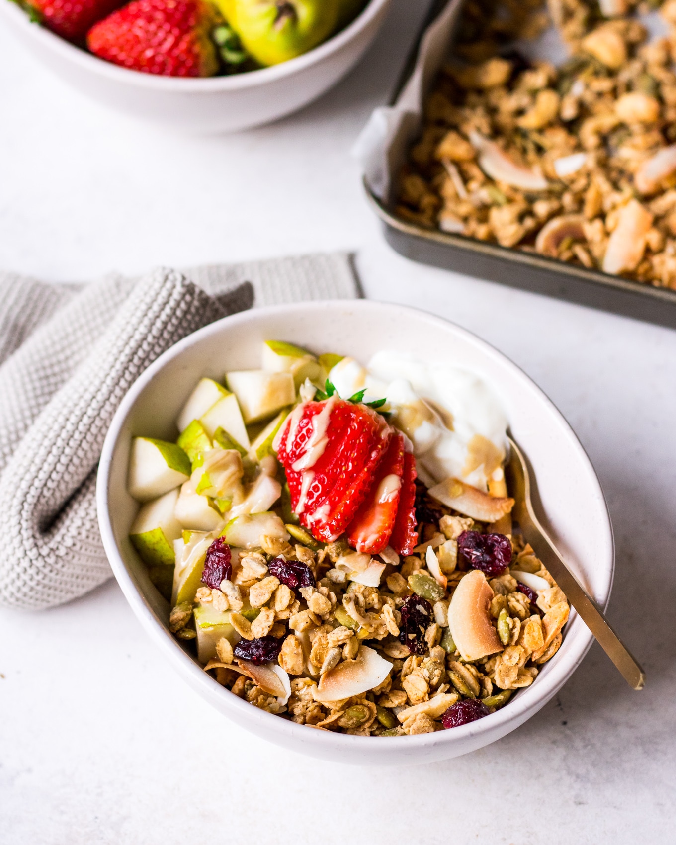 Bowl of maple tahini granola topped with chopped pear and strawberries