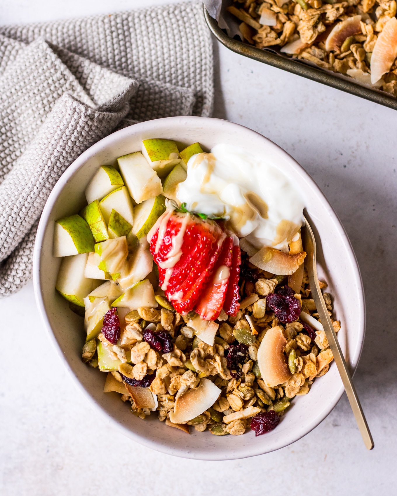 Bowl of maple tahini granola topped with chopped pear and strawberries