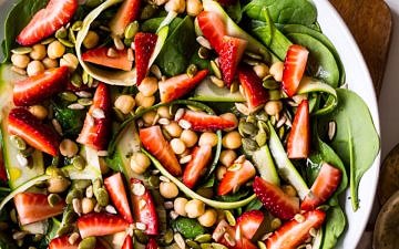 Strawberry, chickpea and spinach salad in a wide bowl on wooden chopping board