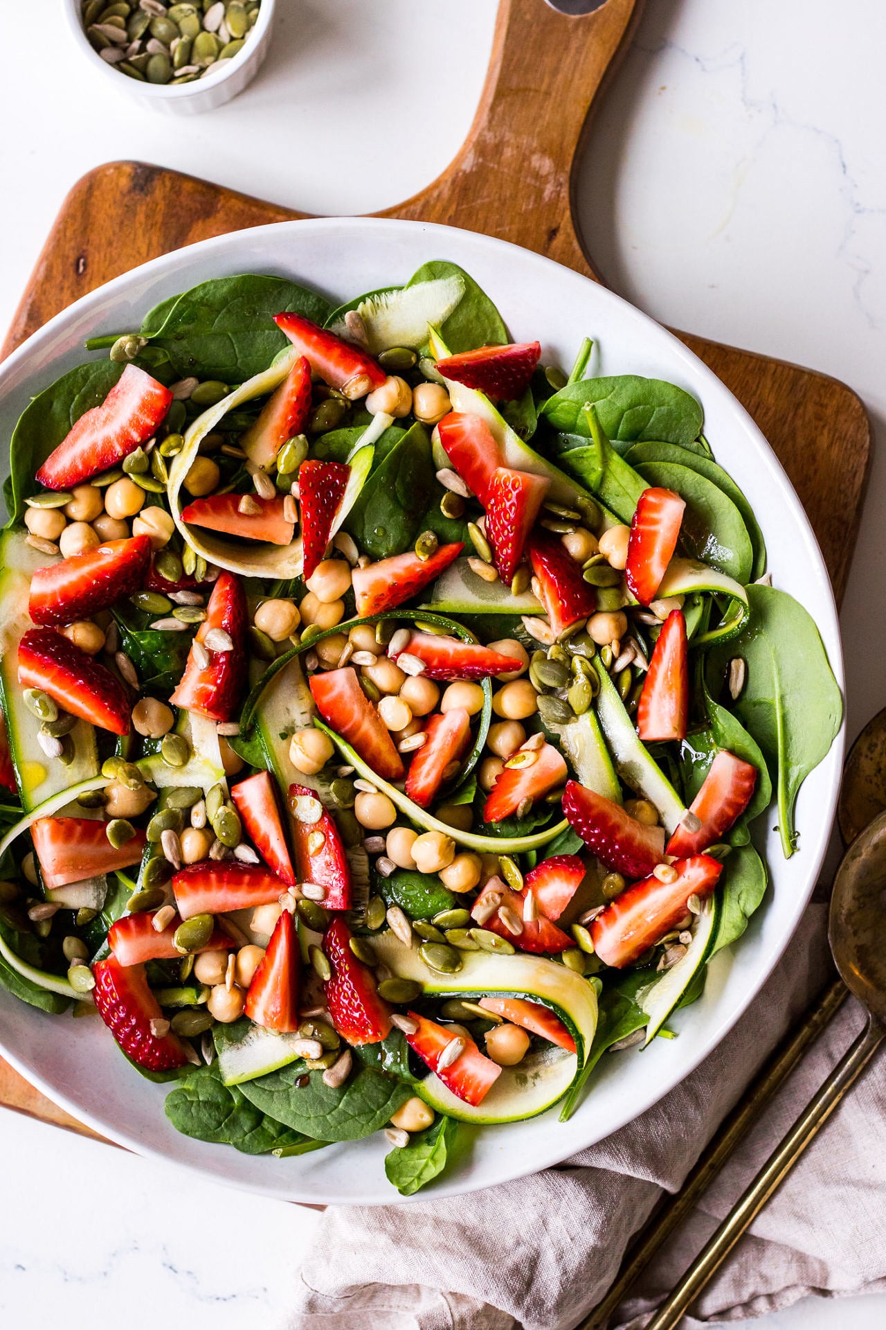 Strawberry, chickpea and spinach salad in a wide bowl on wooden chopping board