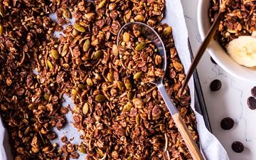 Tray of chocolate olive oil granola with a spoon, small bowl to the side
