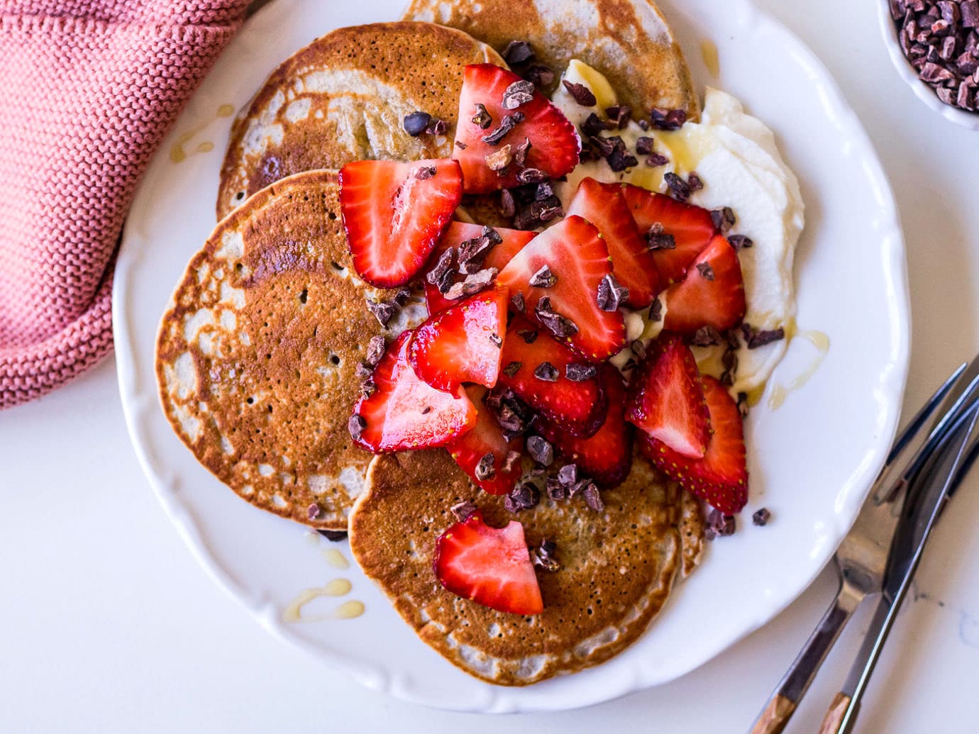 Pequeño plato blanco con panqueques cubierto con fresas y cacao nibs