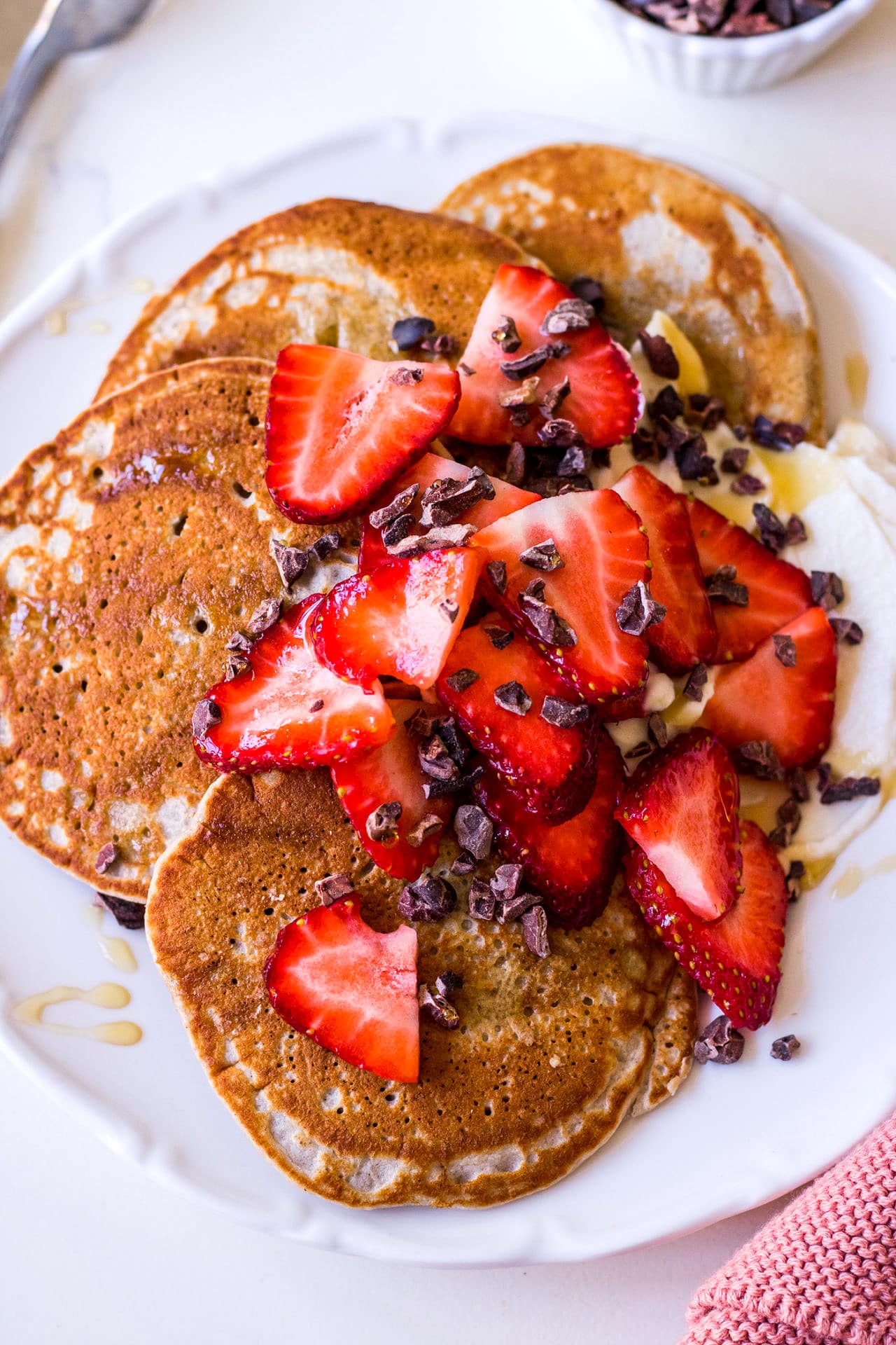 Gros plan de crêpes de sarrasin superposées sur une assiette blanche avec des fraises tranchées et des graines de cacao saupoudrées sur le dessus