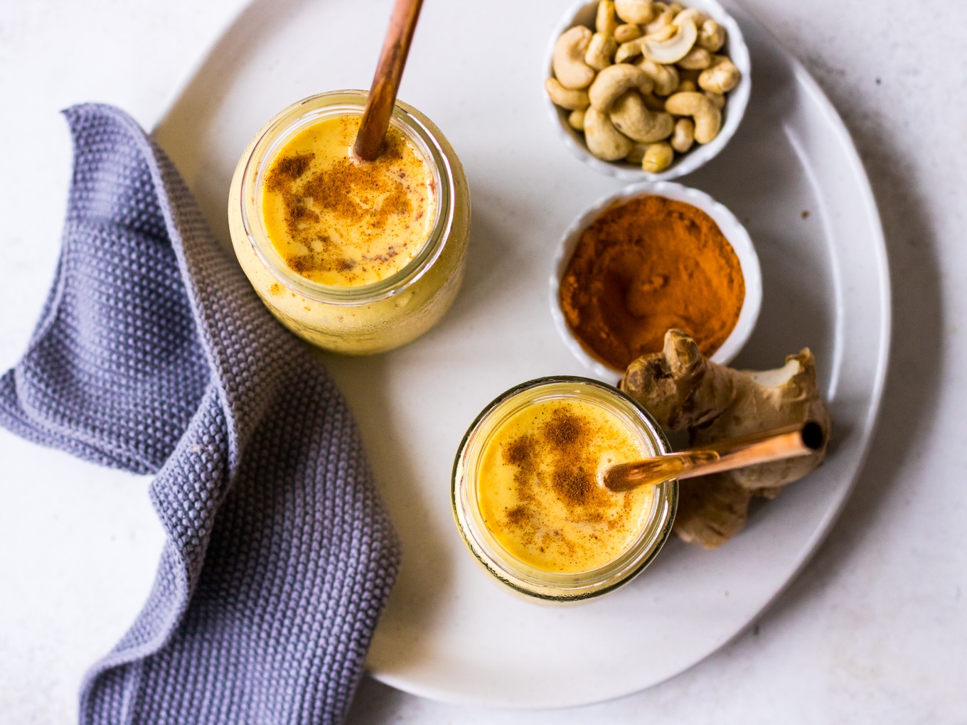 Top down view of turmeric mango smoothie in jars on an irregular white plate