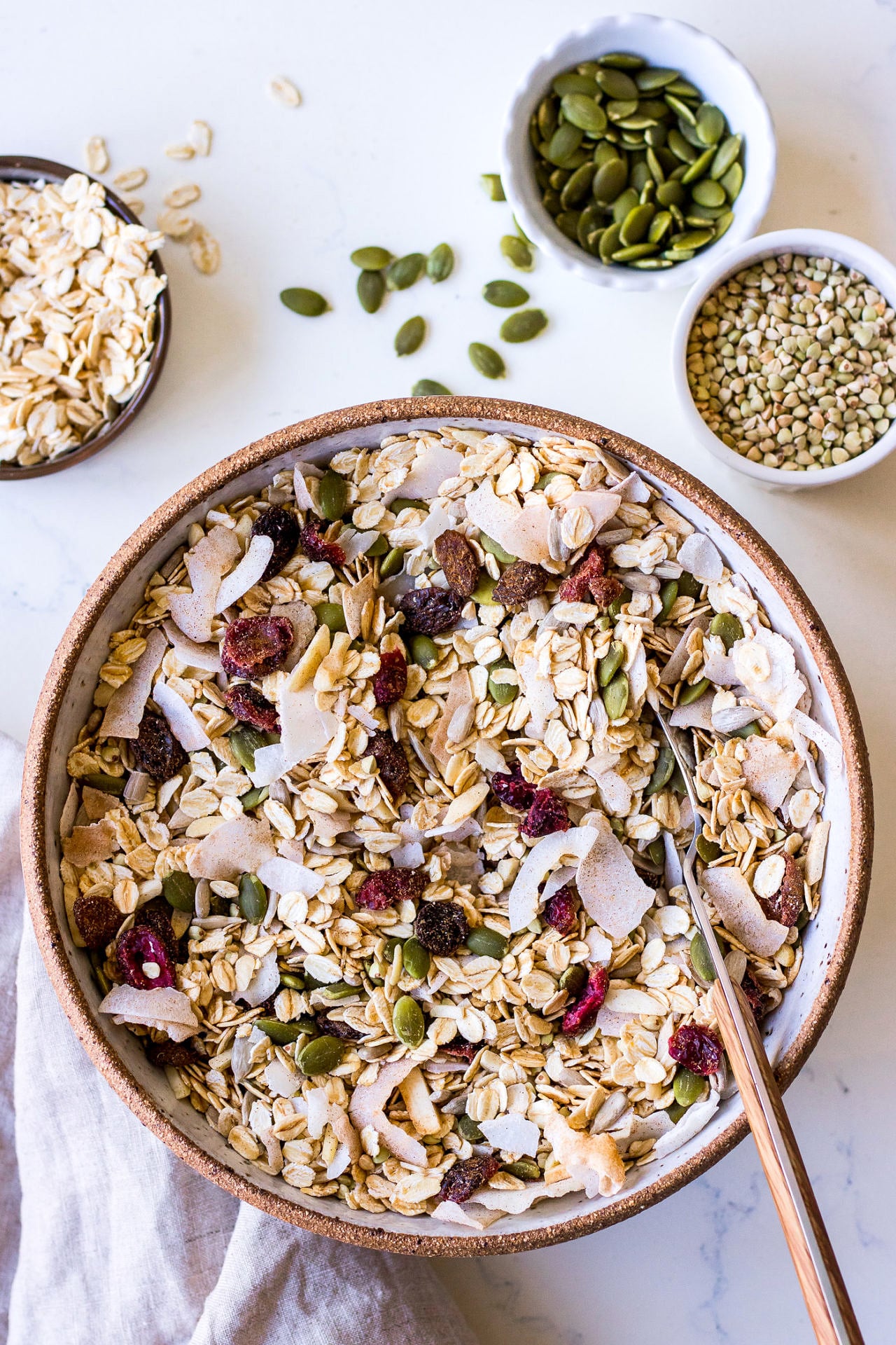 Large ceramic bowl filled with a healthy oat, coconut, pumpkin seed and dried fruit muesli with a wooden spoon sticking out