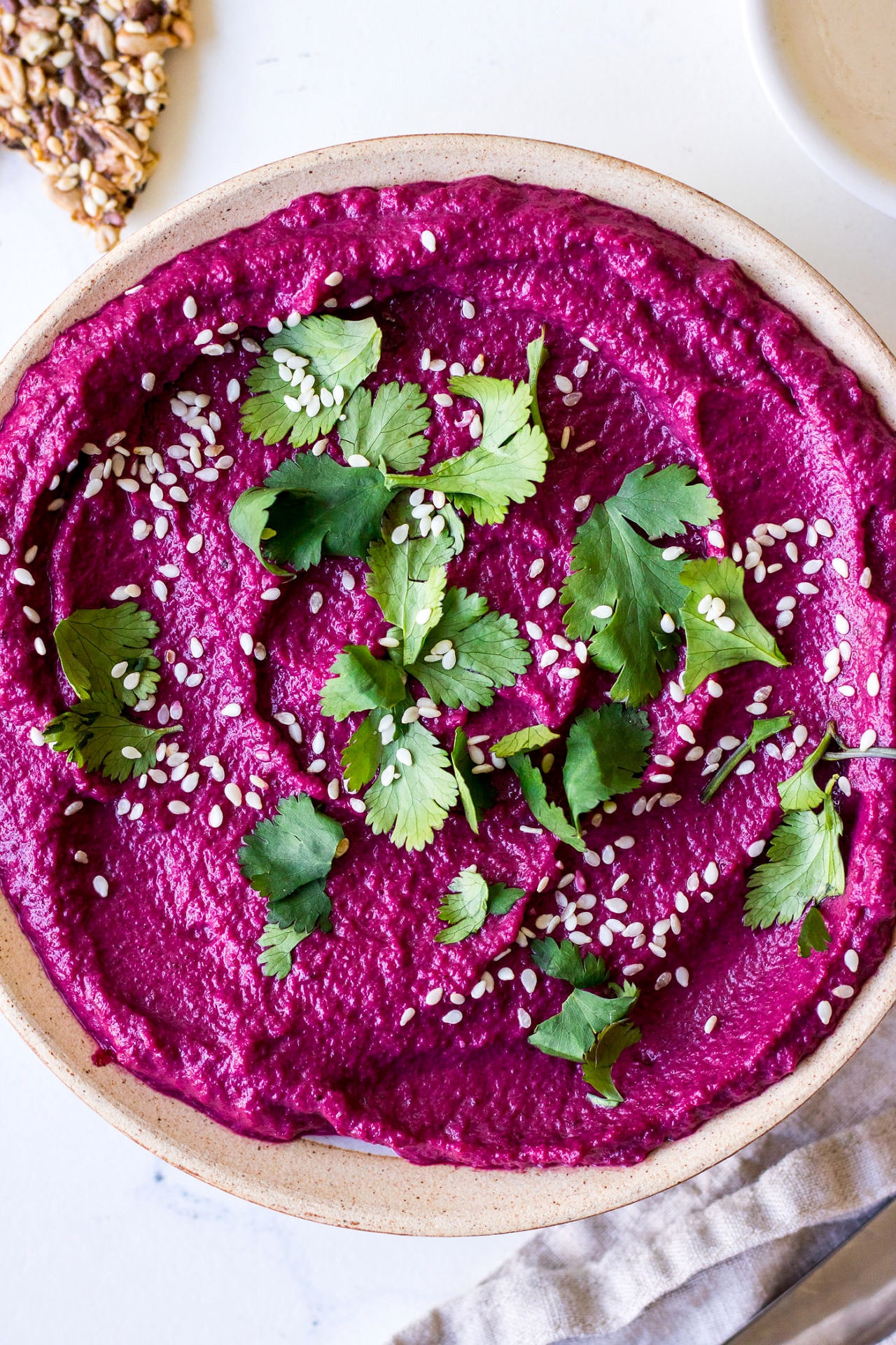 ceramic round dish filled with roasted beet dip and topped with coriander and sesame seeds