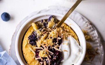 Vanilla mug cake in white ramekin with blueberries, yoghurt and shredded coconut, blue napkin and blueberries