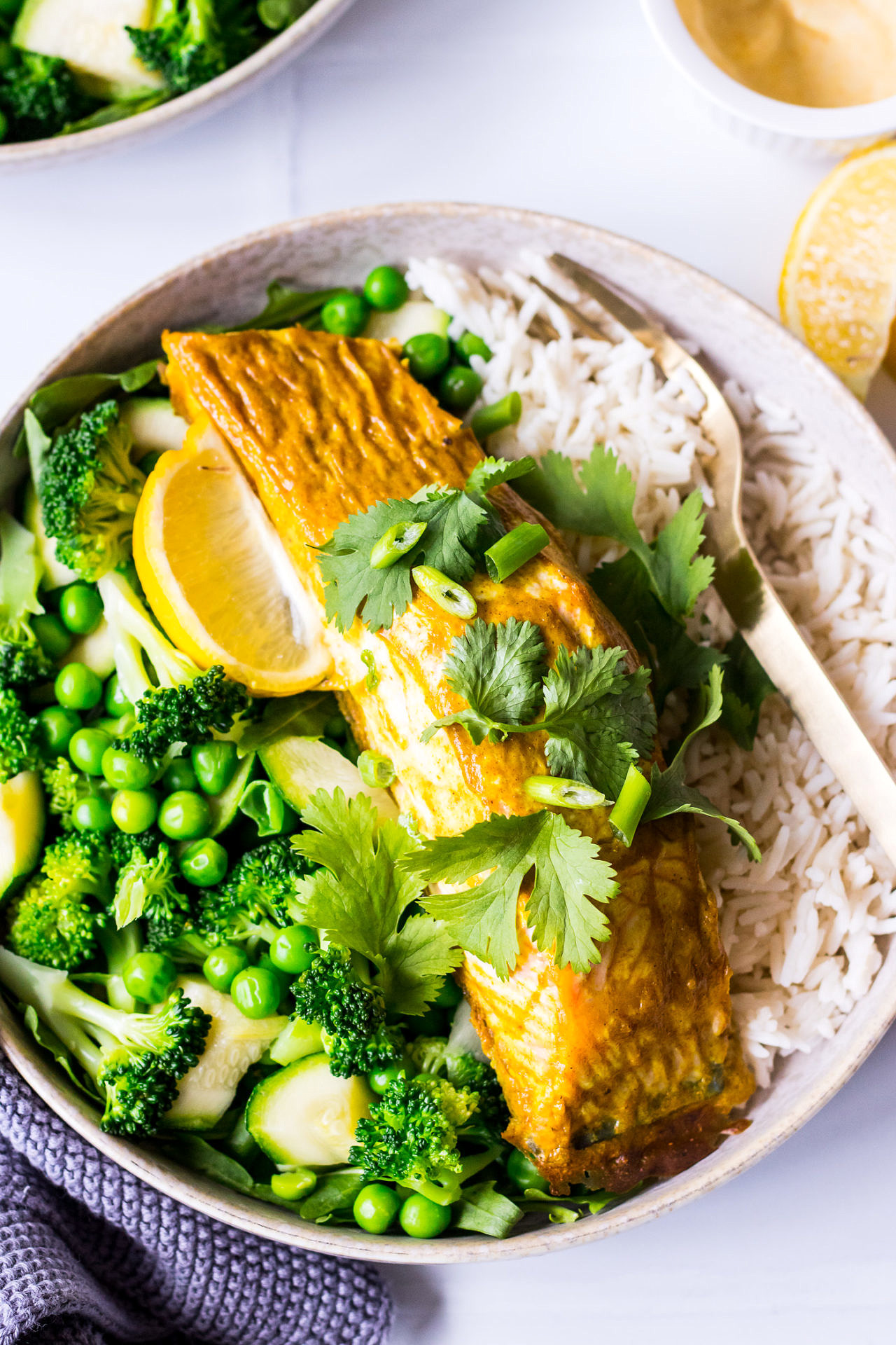 Baked salmon fillet rubbed with curry spice, in a bowl on top of white rice and green vegetables