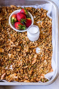Baking tray with granola, strawberries, small jar of milk, wooden spoon