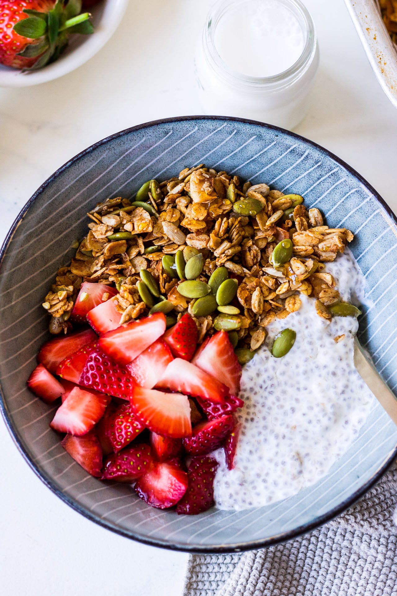 Close up blue striped bowl with creamy chia pudding, chopped strawberries and granola