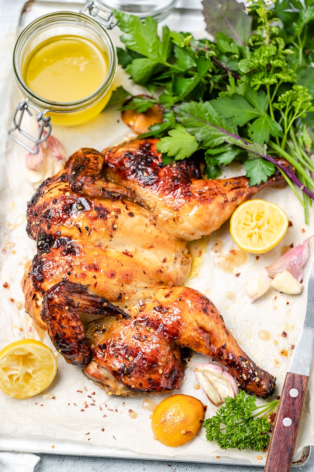 Flattened roast chicken with lemon pieces, fresh parsley and jar of pan juices
