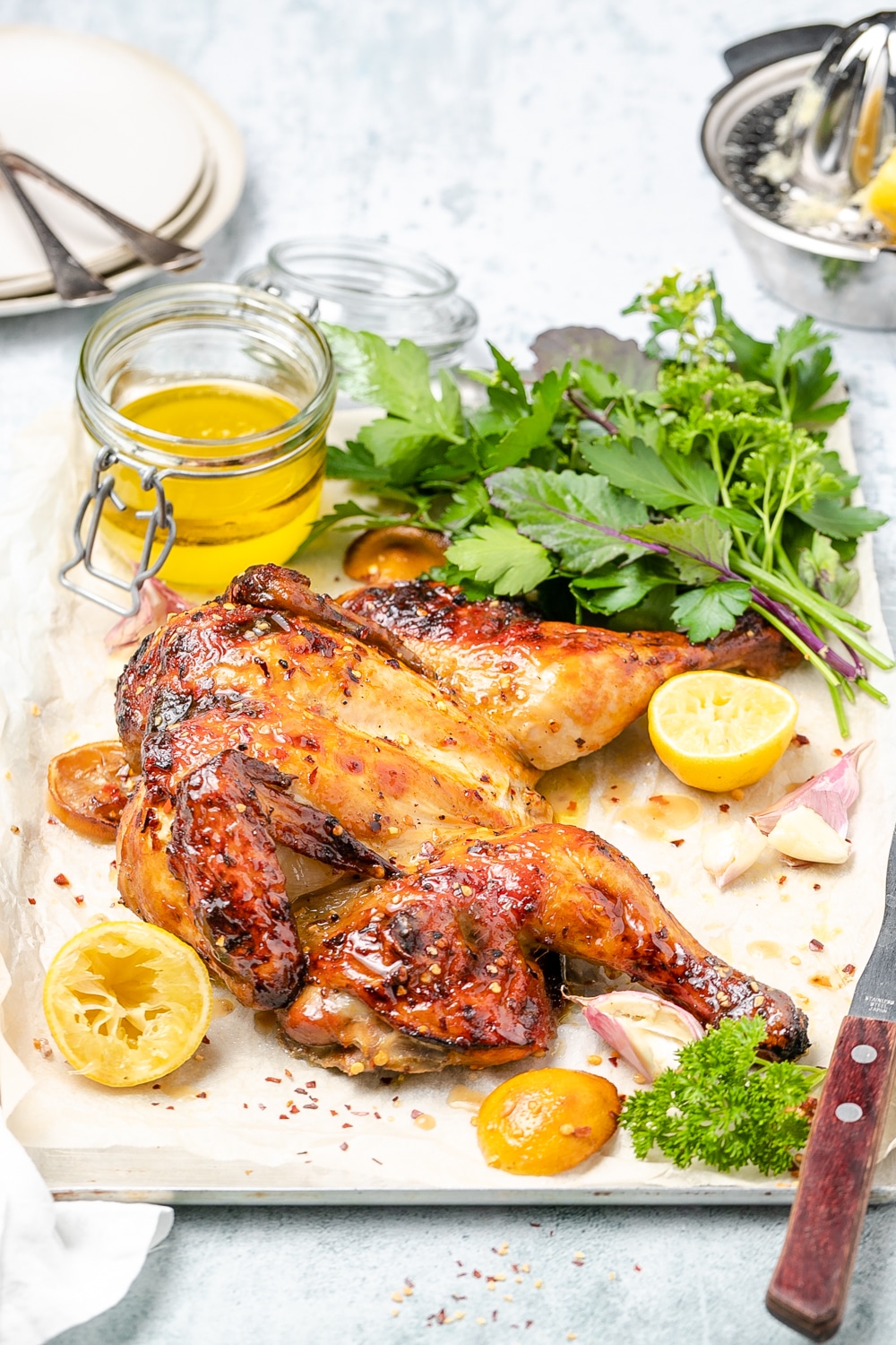 Butterflied roast chicken surrounded by lemons, fresh herbs and small jar of pan juices