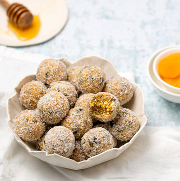 small white scalloped bowl filled with apricot bliss balls, white napkin and honey to side