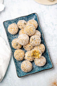 Blue rectangular plate with apricot bliss balls on top rolled in coconut, white table background
