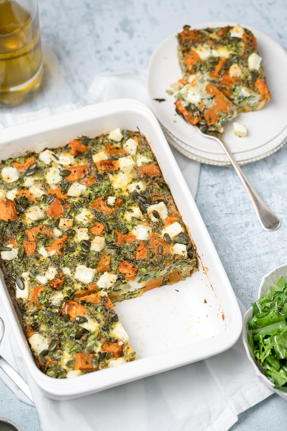 White rectangular baking dish with frittata with feta, sweet potato, broccoli and pumpkin seeds, side plate