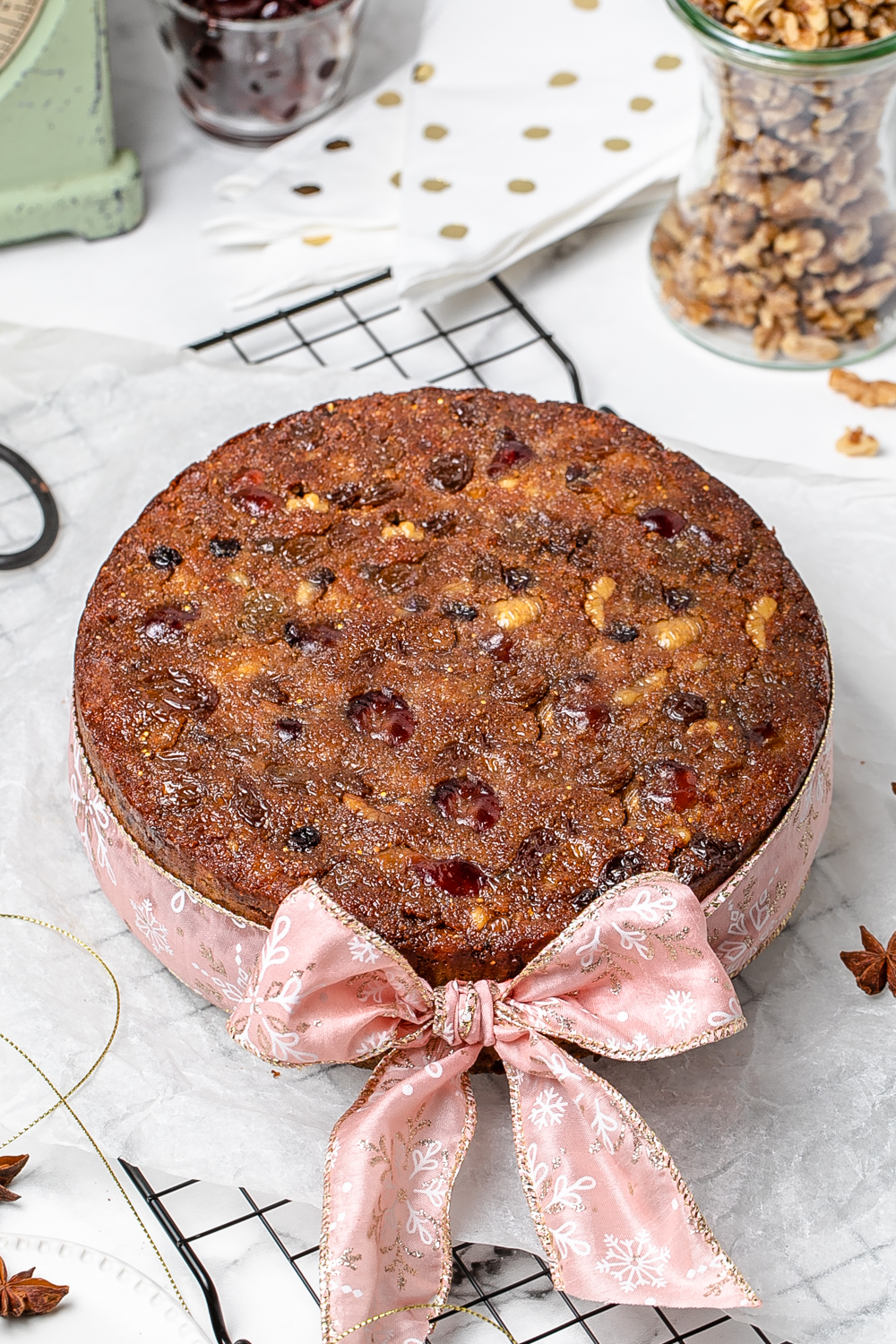 Round Christmas fruit cake with a pink ribbon and bow, sitting on wire baking rack and baking paper
